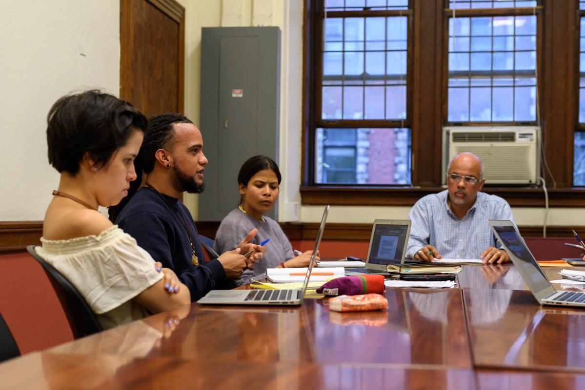 Four people of various races sit around a table with laptops open in front of them.