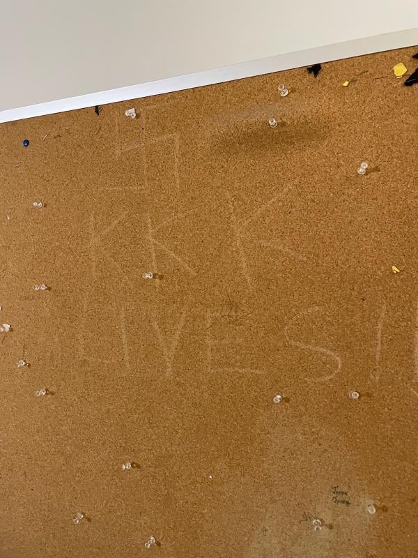A corkboard at Queens College with the words "KKK lives" and a swastika carved into it.