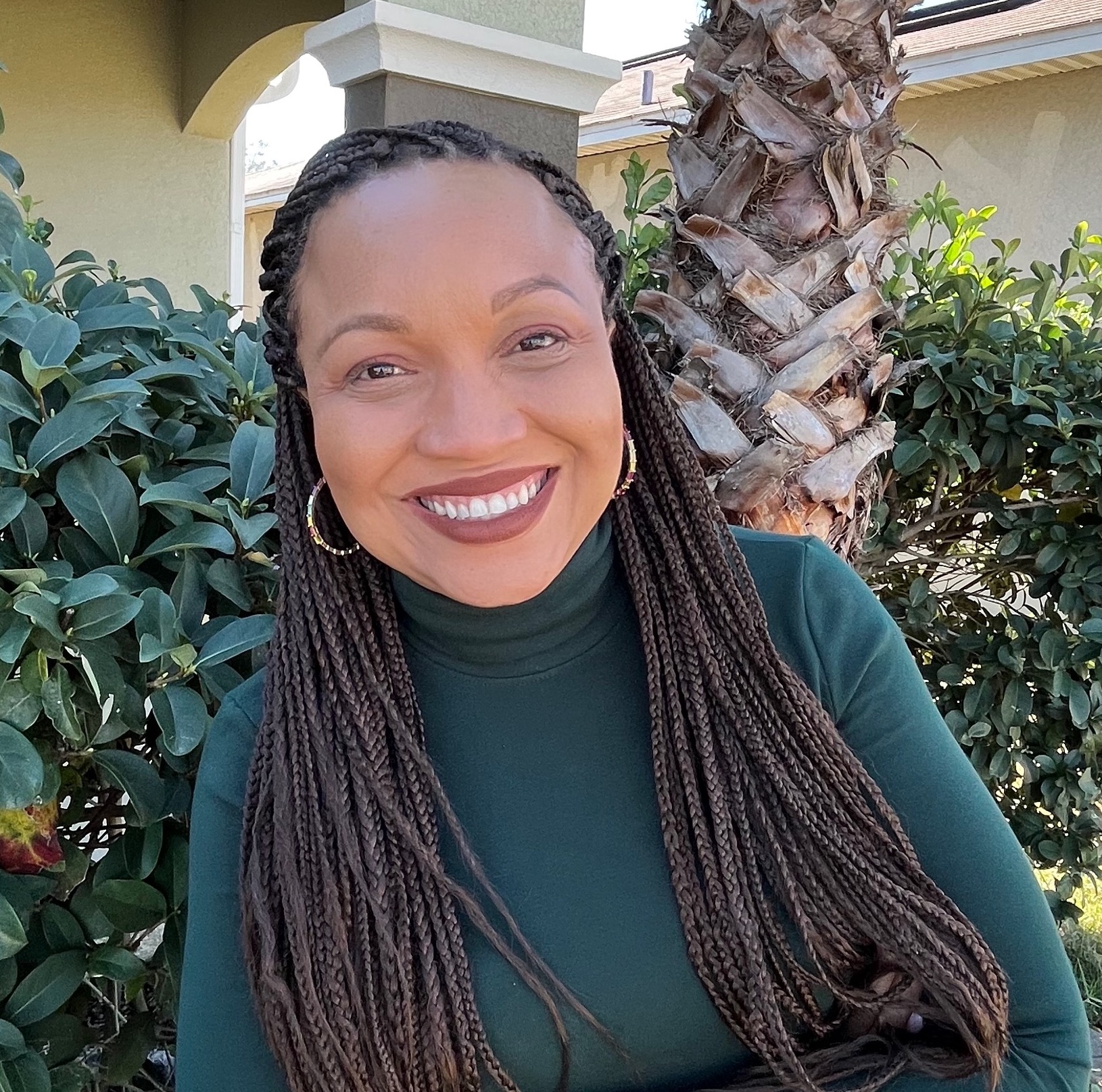 Dientje Francis-Lawrence, a Black woman with her hair in long braids who is wearing hoop earrings and a turtleneck.