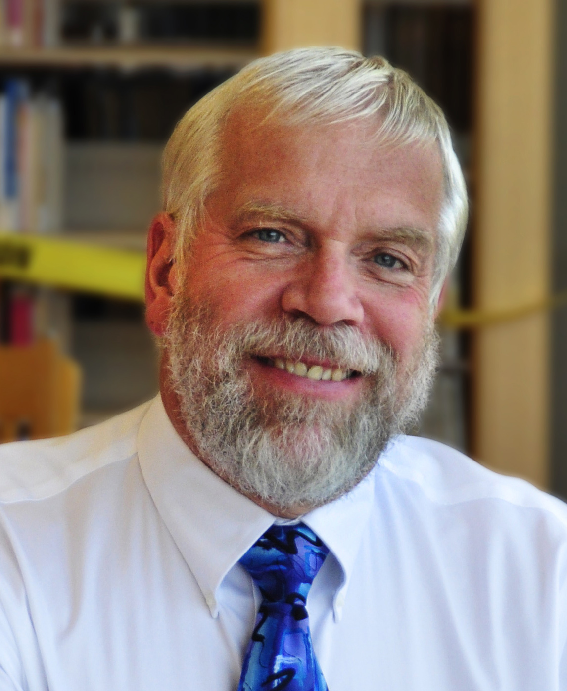 David Lewis, a white man with white hair and a beard wearing a blue necktie.