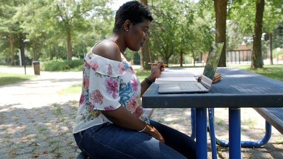 Woman working outdoors on a laptop at a picnic table.