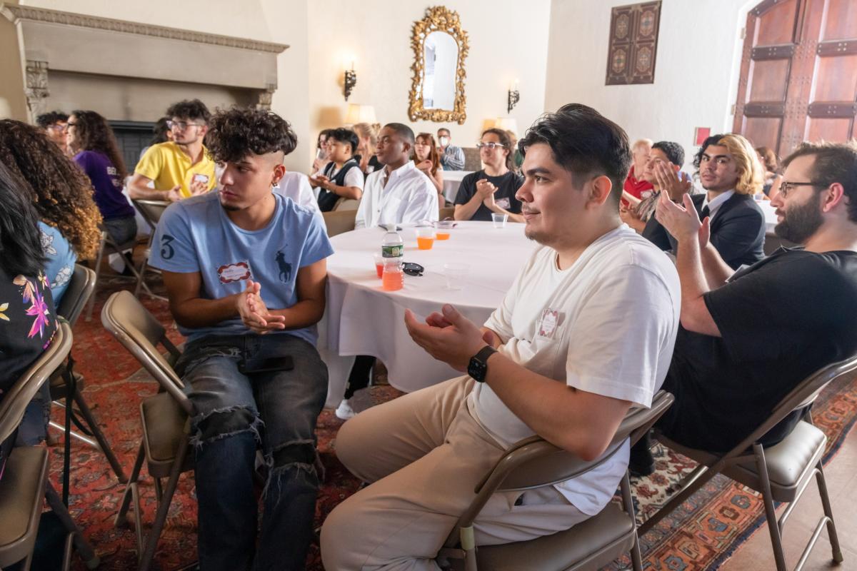 A group of community college students in the Exploring Transfer program at Vassar College sit at tables at a program event and applaud.