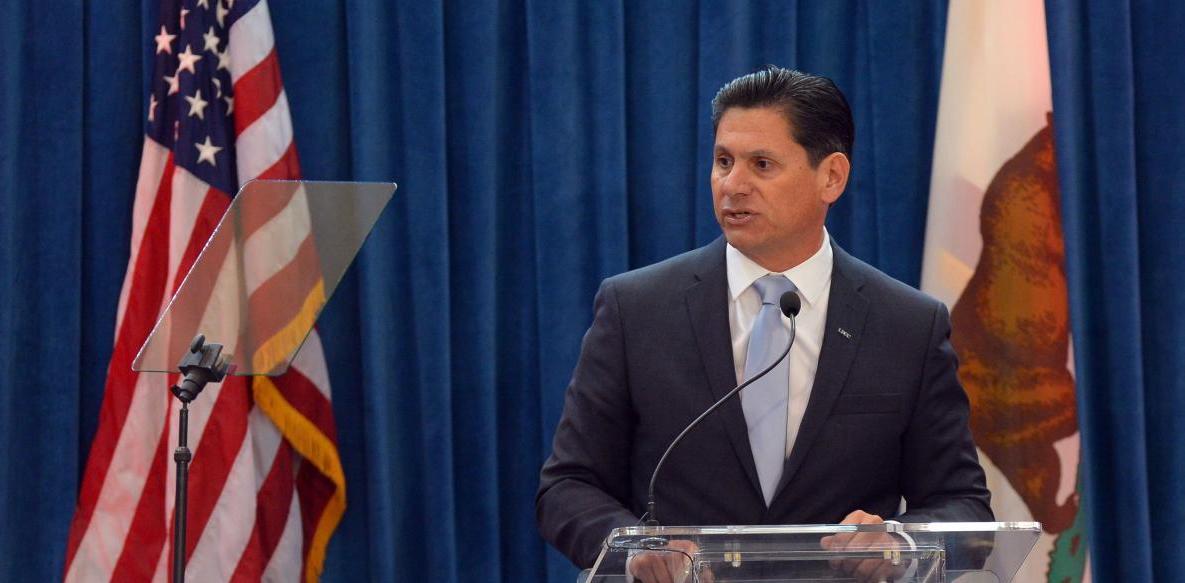 Eloy Ortiz Oakley, chancellor of the California Community Colleges system, speaks at a podium with an American flag to his left and a California flag to his right.