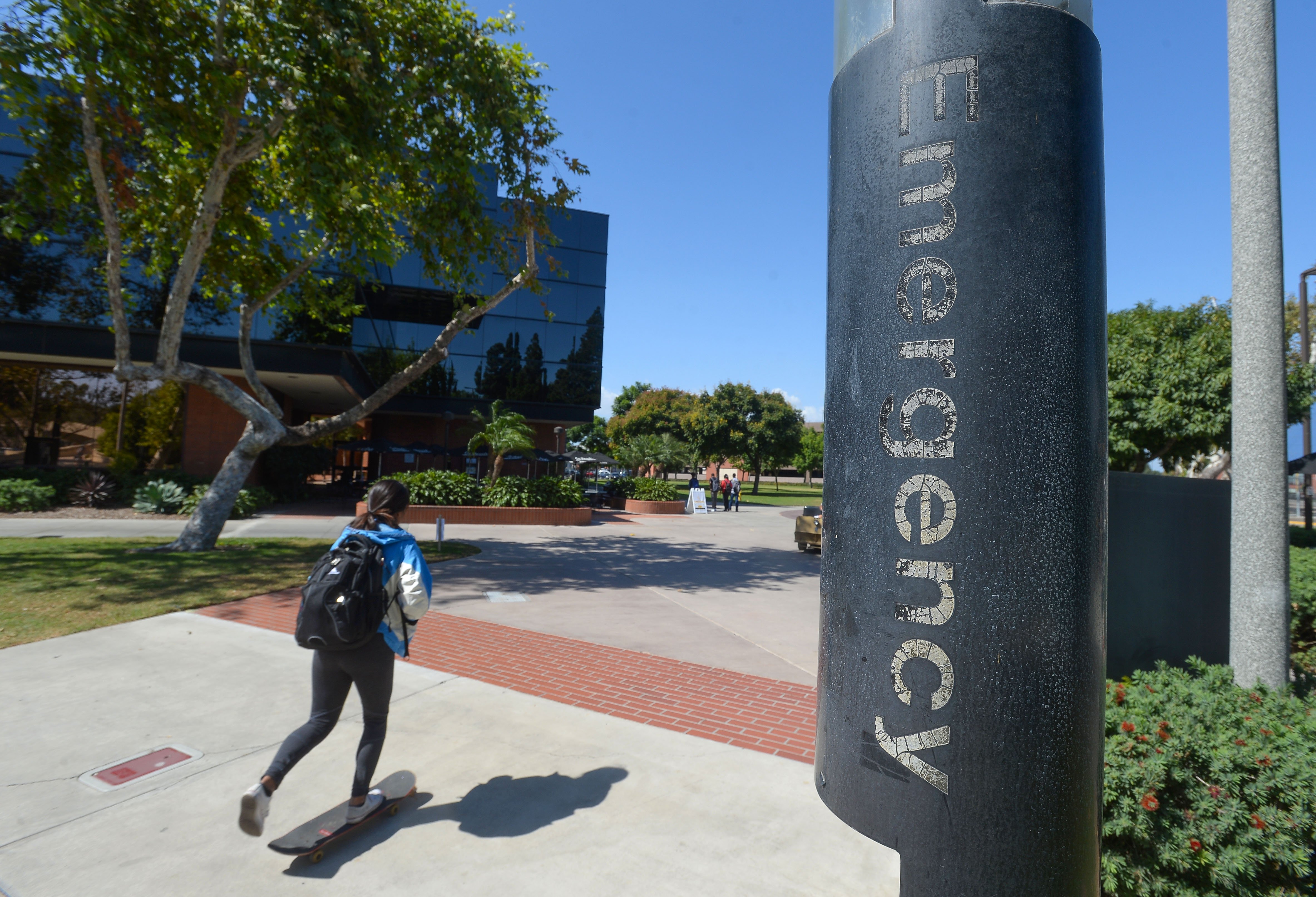 A student on campus next to a light post marked "Emergency."