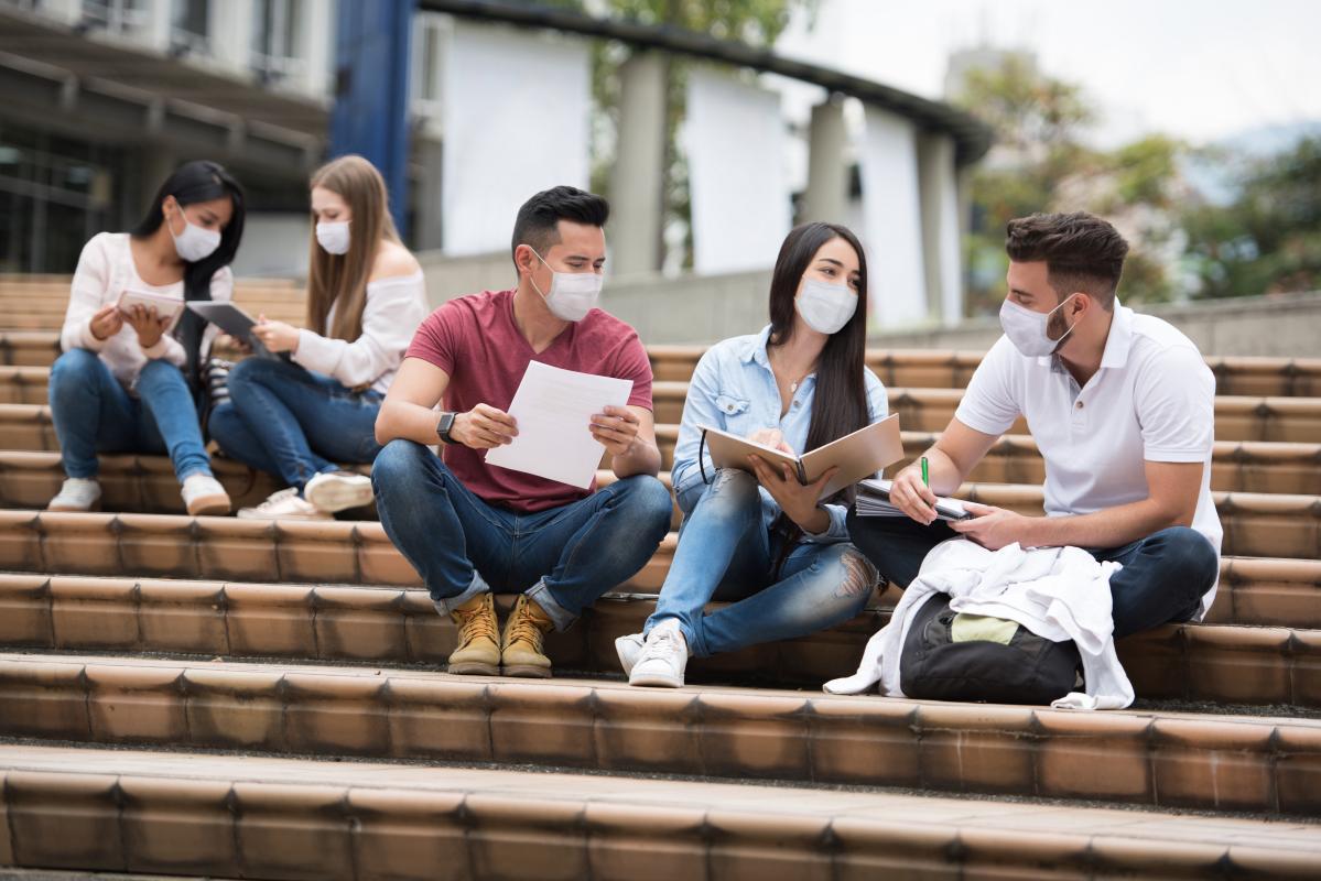 Students in masks sit on the steps of a campus quad.