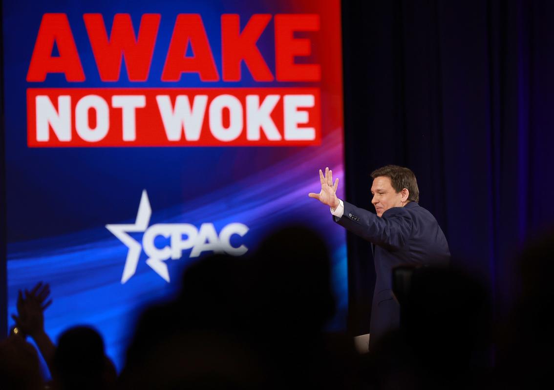 Florida governor Ron DeSantis at a Conservative Political Action Conference event, in front of a banner reading "Awake, not woke."