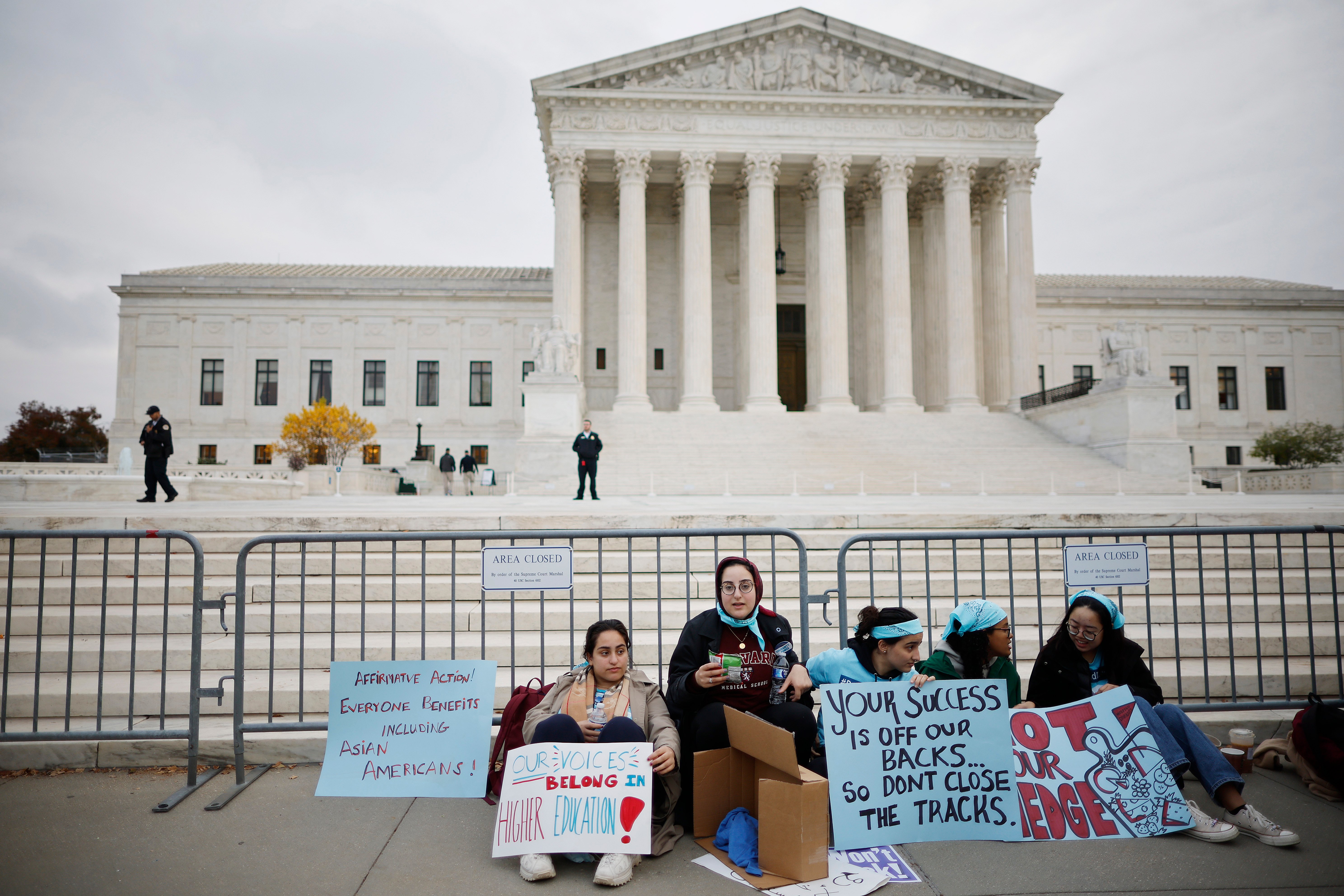 Students sit on the ground in front of the Supreme Court with signs supporting affirmative action.