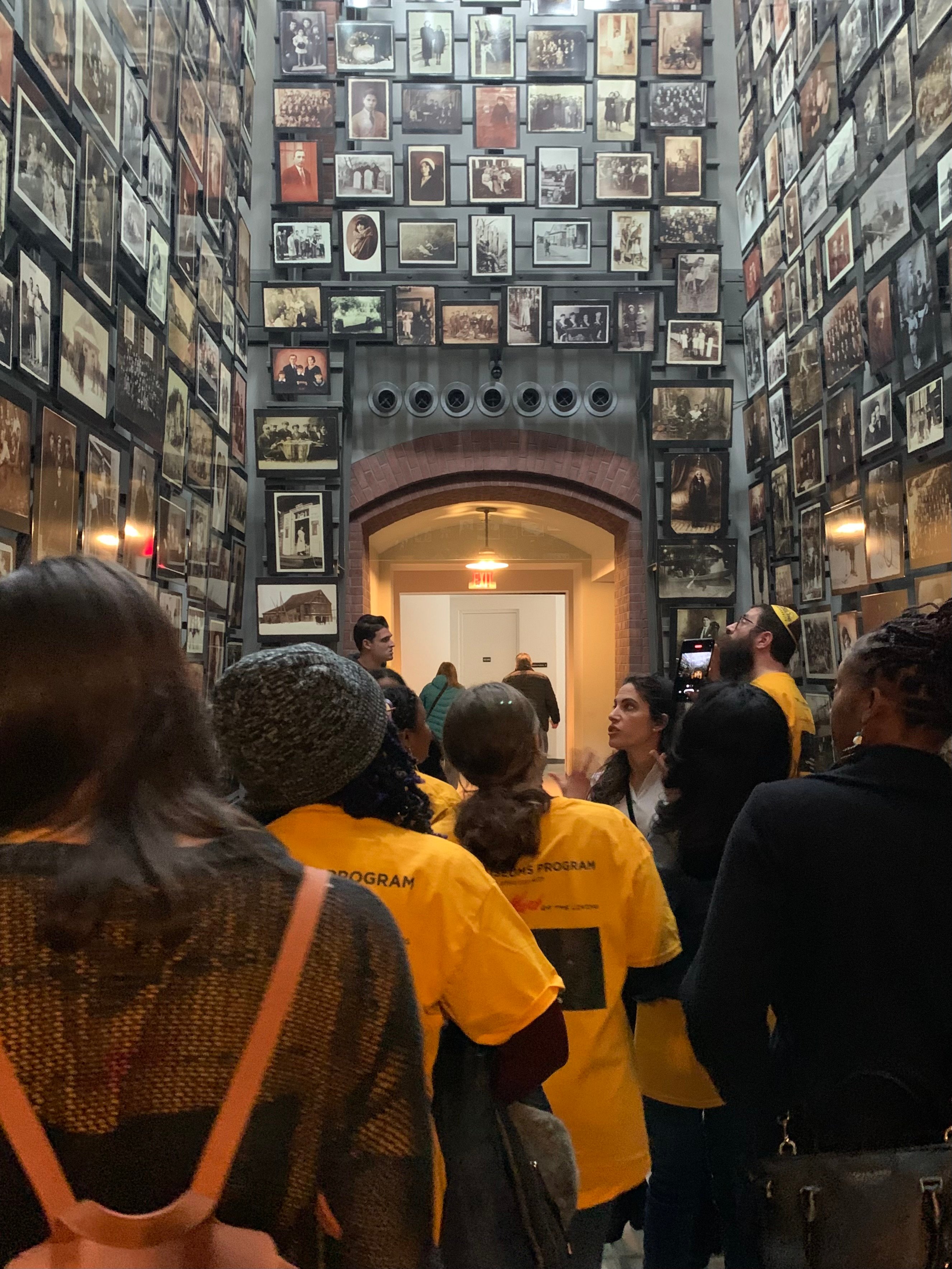 Adelphi University students in yellow shirts walk through a hallway of portraits of people killed in the Holocaust at the U.S. Holocaust Memorial Museum. 