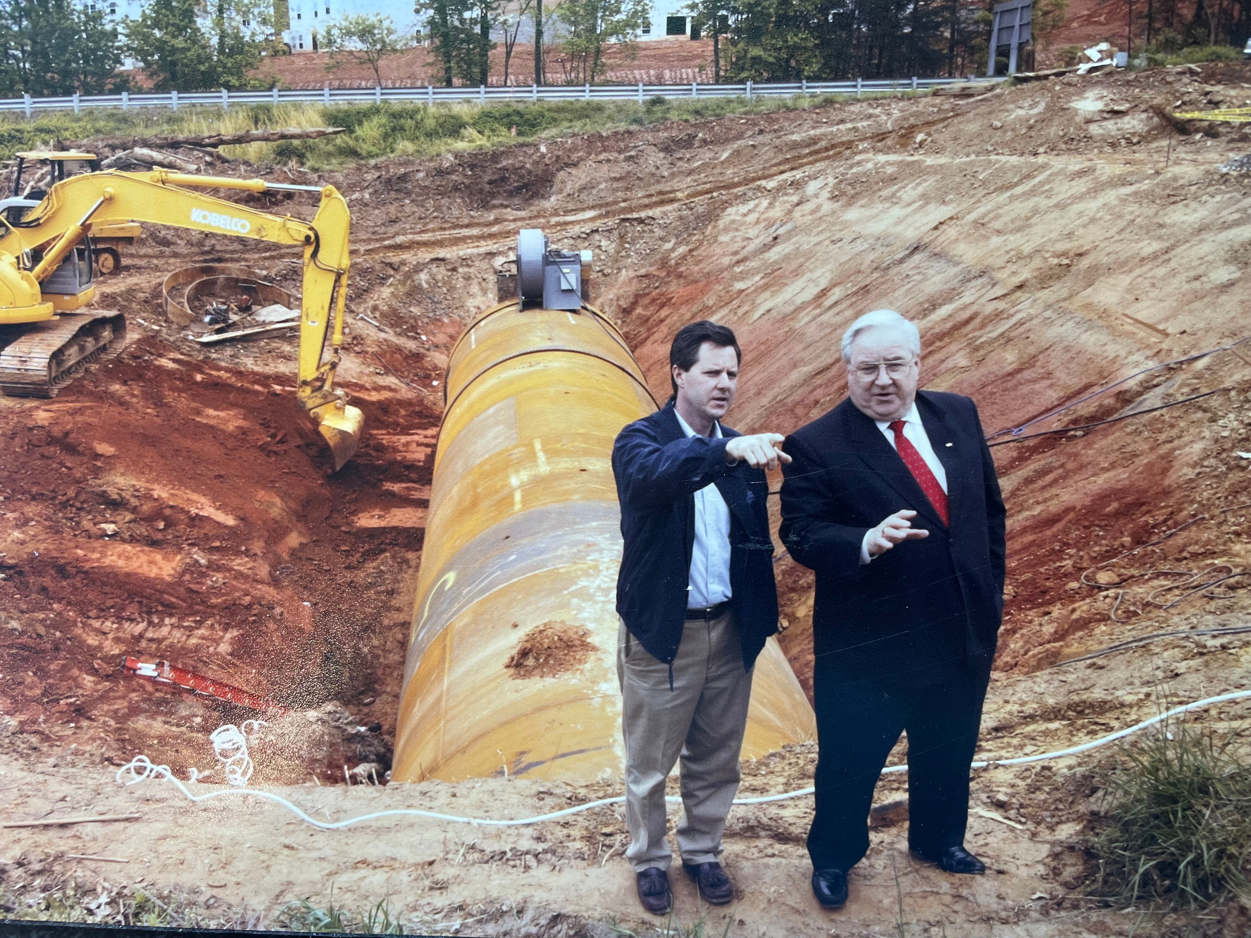 Jerry Falwell Jr. and his father stand in the middle of a construction site, in front of a yellow bulldozer.