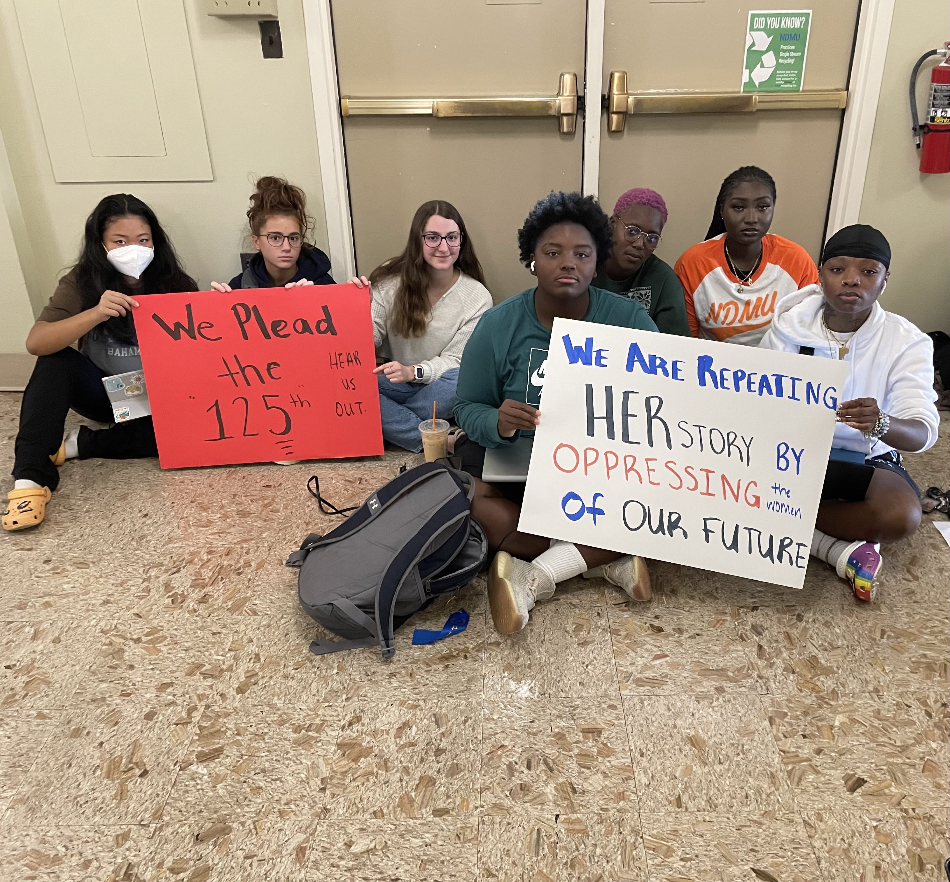 Women students of various races hold up handmade signs that read "We plead the 125th" and "We are repeating HER story by oppressing the women of our future."