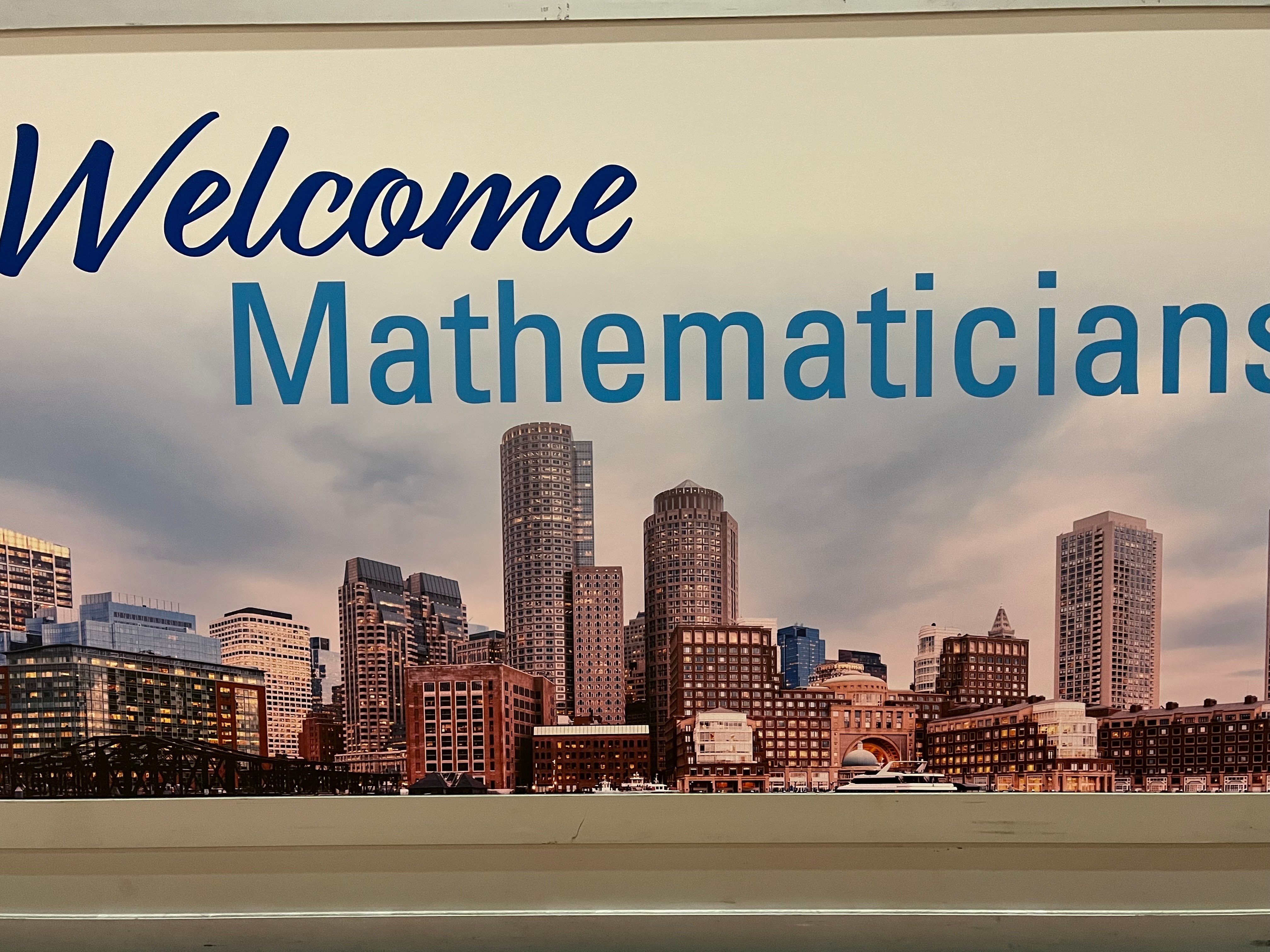A photo of a welcome message at the 2023 Joint Mathematics meetings held in Boston that says, “Welcome Mathematicians” in the sky above the Boston skyline. 