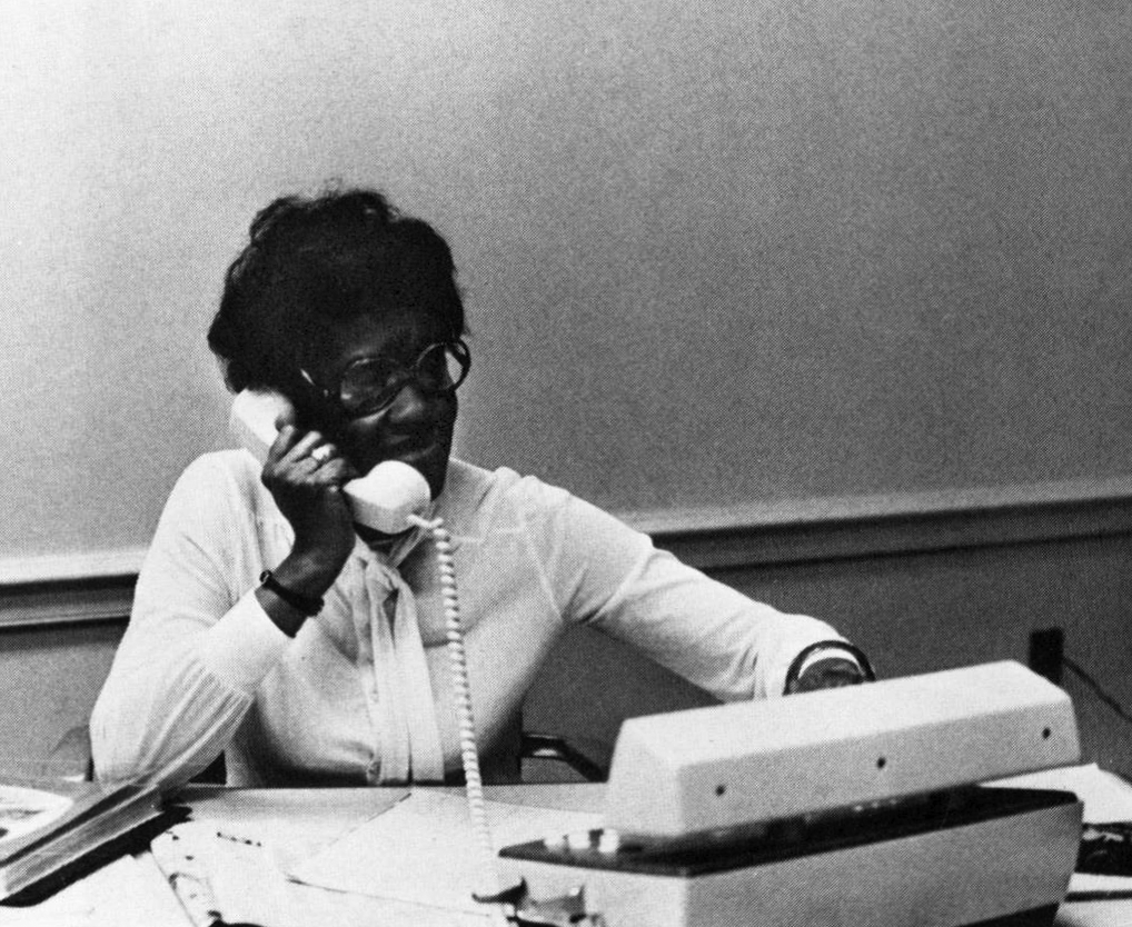 Gözlüklü siyahi bir kadın olan Jewel Bell, siyah beyaz bir fotoğrafta telefonda konuşuyor.