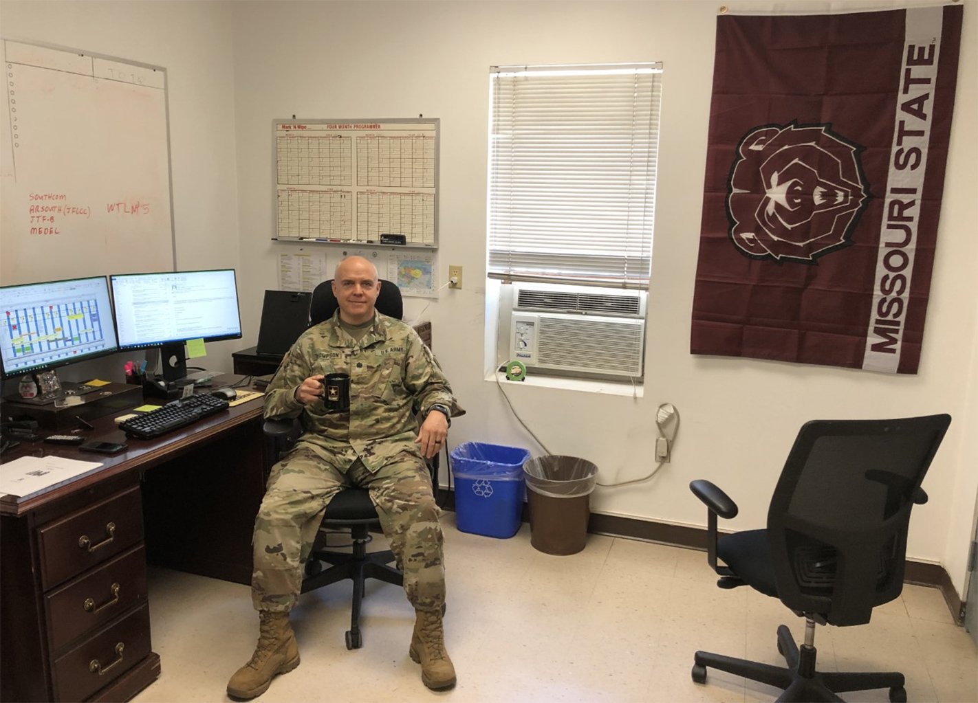 Kip Thompson sits in front of his teaching workstation with two monitors while wearing the uniform for his military assignment in Honduras.