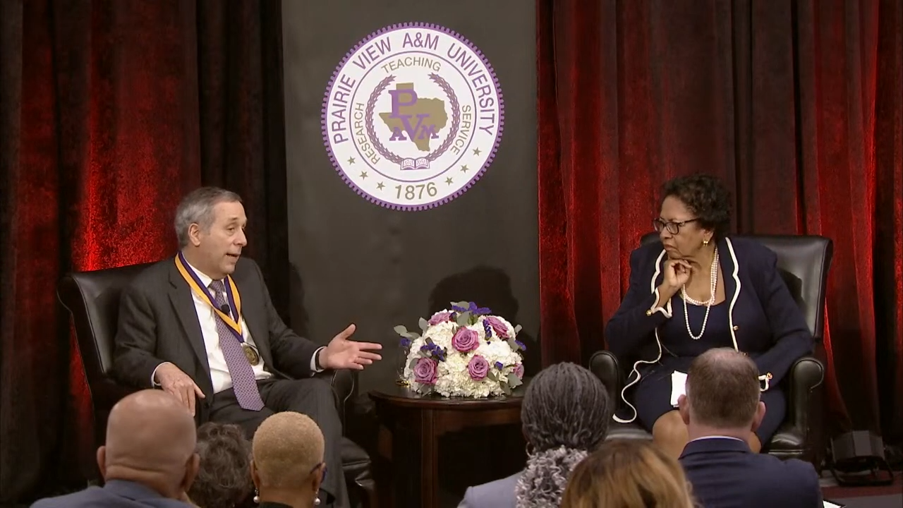 A picture of Harvard president Lawrence Bacow and Ruth Simmons sitting on a stage and speaking to an audience at Prairie View A&M.