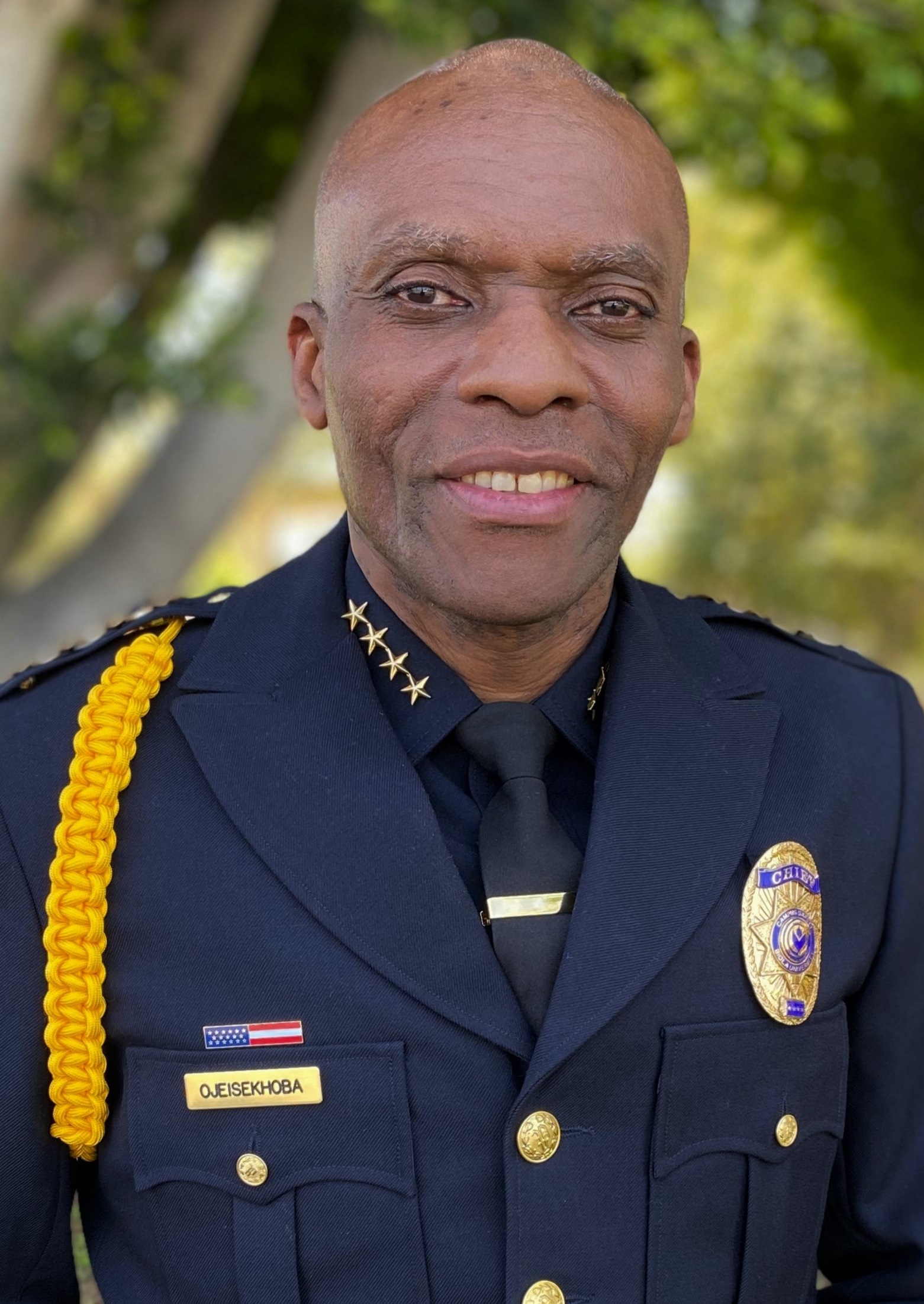John Ojeisekhoba, a bald Black man wearing a police uniform.