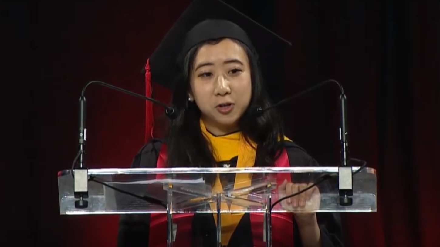 Shuping Yang, wearing academic regalia, speaks at the University of Maryland, College Park.