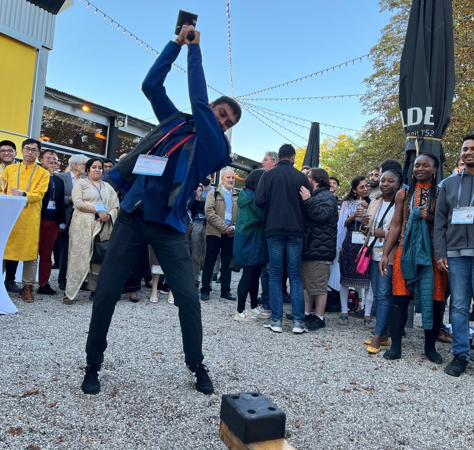 Shwetak Patel, a man with brown skin and dark hair wearing a blue jacket, swings a hammer over his head, bringing it down on a test-of-strength machine like you'd find at a carnival.