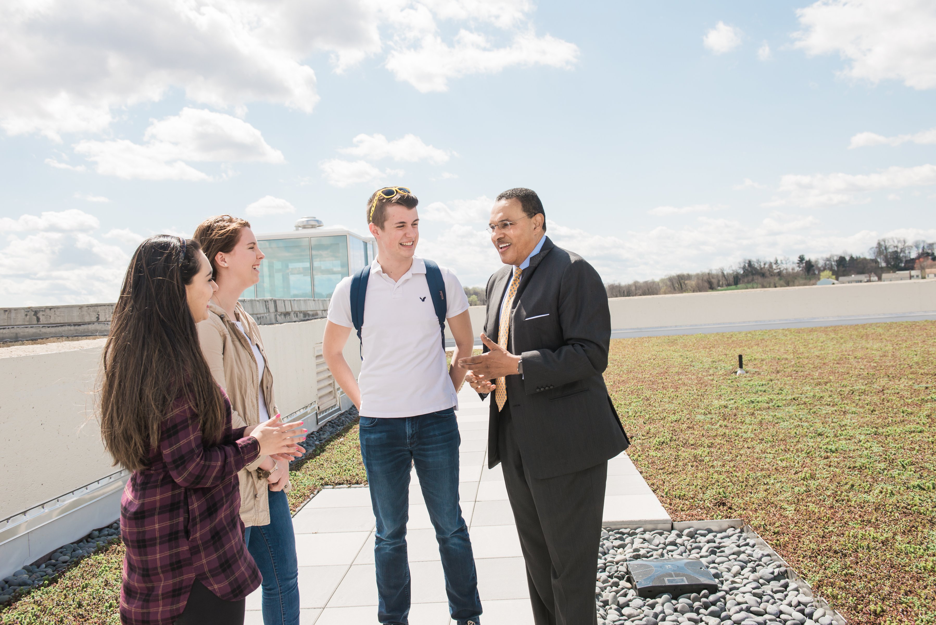 Freeman Hrabowski, a Black man with short hair wearing glasses, talks to three white students.