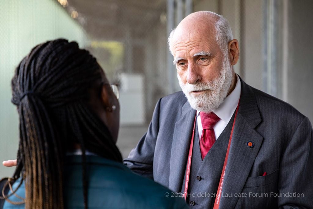 Vinton Cerf, an older white man with a white beard, speaks to a person with long dark hair whose back is to the camera.