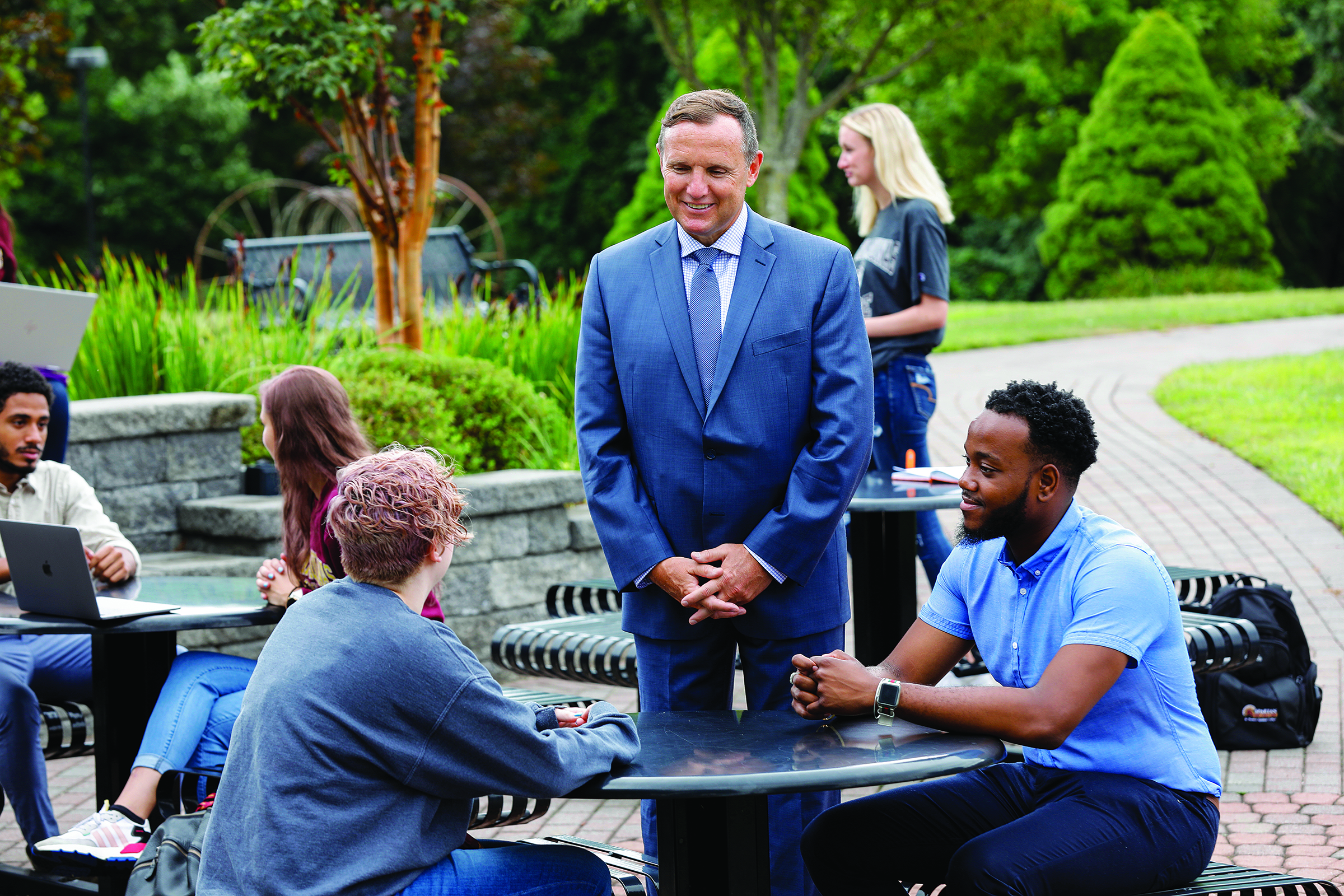 Daly stands next to a table of students outside and chats with them. Photo courtesy of St. Thomas Aquinas College