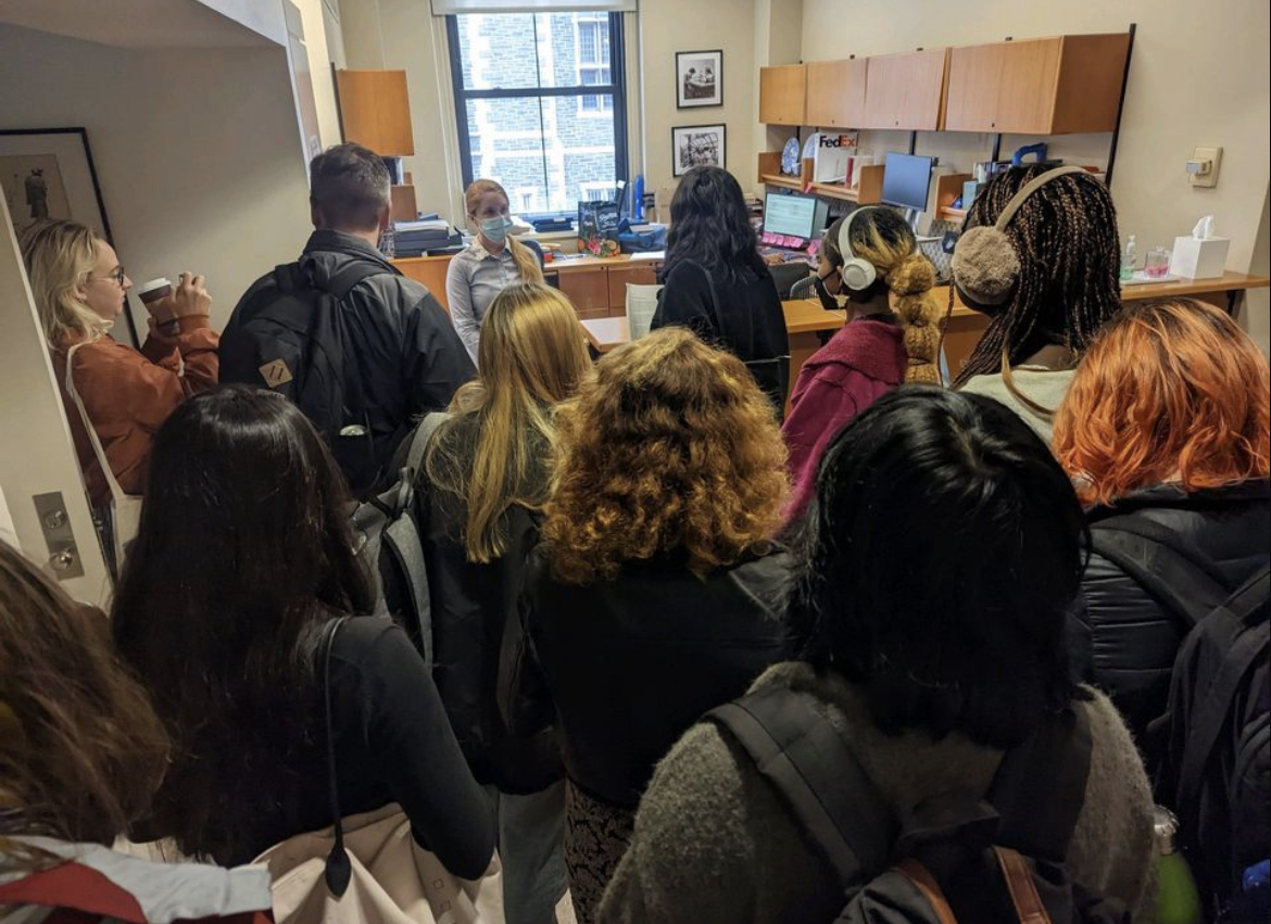 A group of people, some wearing masks, are crowded into a small office.