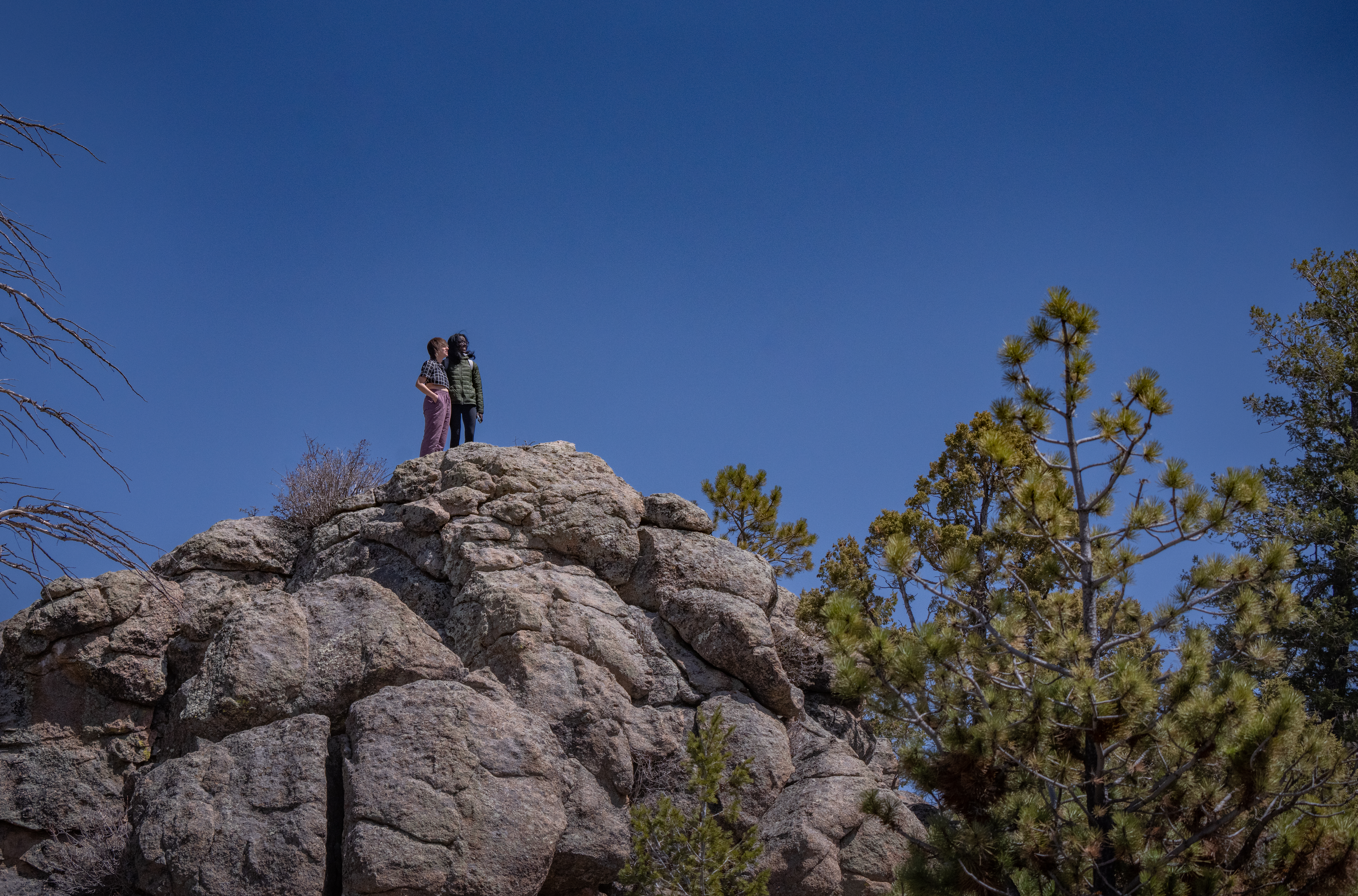 Two people stand on a rock precipice against a blue sky.