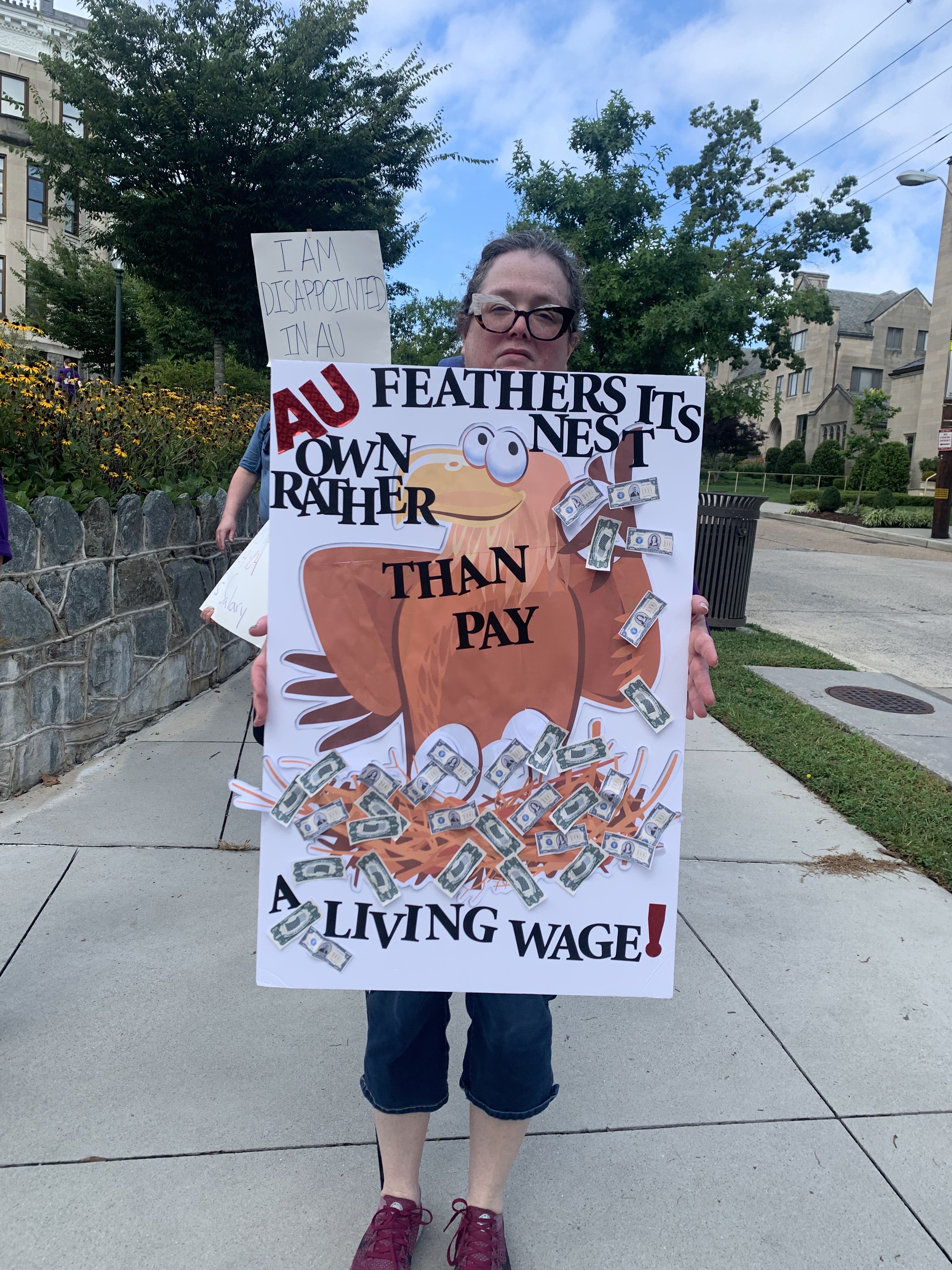 A striking staff member holds a sign that says "AU feathers its own nest rather than pay a living wage!"