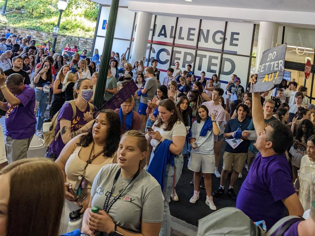 A huge group of students, some wearing masks and many wearing the purple shirts of SEIU, are gathered in the atrium of Bender Hall.