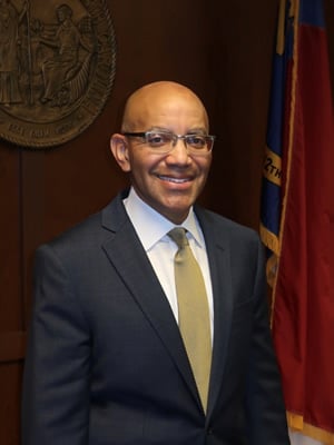 Thomas Stith, a light-skinned Black man wearing glasses and a suit.